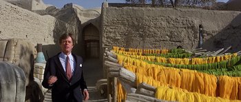 Movie still from “Caravans” (1978), directed by James Fargo – A man in a suit and tie standing in front of yellow umbrellas; Medium shot, Low angle