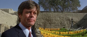 Movie still from “Caravans” (1978), directed by James Fargo – A person wearing a suit and tie; Close Up shot, Low angle