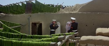 Movie still from “Caravans” (1978), directed by James Fargo – A group of men standing next to each other near a building; Wide shot, Over the shoulder angle
