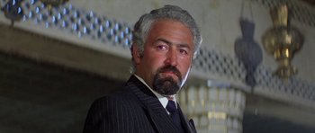 Movie still from “Caravans” (1978), directed by James Fargo – A man in a suit and tie with a white beard; Close Up shot, Low angle