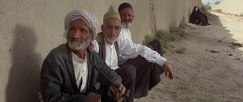Movie still from “Caravans” (1978), directed by James Fargo – A group of men sitting next to each other on the ground; Medium shot, High angle
