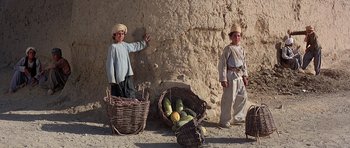 Movie still from “Caravans” (1978), directed by James Fargo – Two men standing next to a wall with baskets of fruit; Wide shot, Low angle