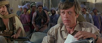 Movie still from “Caravans” (1978), directed by James Fargo – A man sitting in the back of a truck while others look on; Close Up shot, Over the shoulder angle