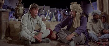 Movie still from “Caravans” (1978), directed by James Fargo – Two men sitting on the ground talking to each other; Medium shot, Over the shoulder angle