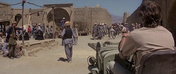 Movie still from “Caravans” (1978), directed by James Fargo – A group of people walking around a dirt road; Wide shot, Over the shoulder angle