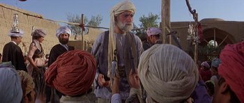 Movie still from “Caravans” (1978), directed by James Fargo – An old man with a long white beard is talking to a group of people; Medium shot, Over the shoulder angle