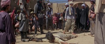 Movie still from “Caravans” (1978), directed by James Fargo – A group of men standing next to a man laying on the ground; Wide shot, High angle