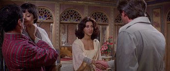 Movie still from “Caravans” (1978), directed by James Fargo – A woman shaking hands with a man in front of an ornate room; Medium shot, Over the shoulder angle