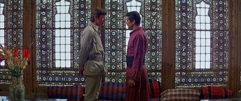 Movie still from “Caravans” (1978), directed by James Fargo – Two men standing next to each other in front of a stained glass window; Medium shot, Over the shoulder angle