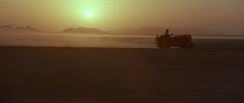 Movie still from “Caravans” (1978), directed by James Fargo – A person riding a boat on a body of water at sunset; Extreme Wide shot, Low angle