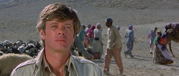 Movie still from “Caravans” (1978), directed by James Fargo – A man standing in front of a group of people; Close Up shot, Low angle