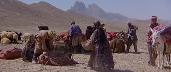 Movie still from “Caravans” (1978), directed by James Fargo – A group of people sitting on top of a dirt field; Extreme Wide shot, High angle