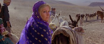 Movie still from “Caravans” (1978), directed by James Fargo – A woman in a purple scarf standing next to a donkey; Medium shot, Low angle