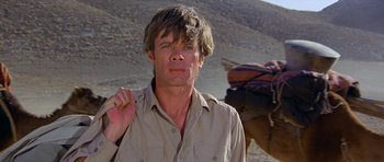 Movie still from “Caravans” (1978), directed by James Fargo – A man standing in the desert with a horse behind him; Close Up shot, Low angle