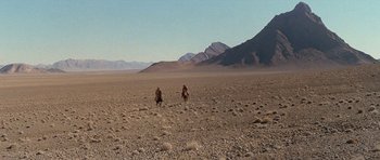 Movie still from “Caravans” (1978), directed by James Fargo – A couple of people riding on the back of a camel; Extreme Wide shot, High angle