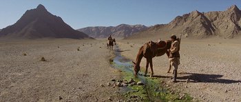 Movie still from “Caravans” (1978), directed by James Fargo – A man on a horse drinks water from a stream; Extreme Wide shot, High angle