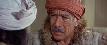 Movie still from “Caravans” (1978), directed by James Fargo – An older man with a mustache wearing a red turban; Close Up shot, Over the shoulder angle