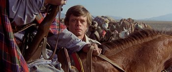 Movie still from “Caravans” (1978), directed by James Fargo – A man on a horse in the middle of a crowd; Close Up shot, Low angle