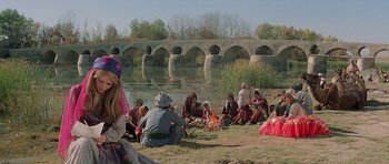 Movie still from “Caravans” (1978), directed by James Fargo – A group of people sitting on the grass next to a body of water; Wide shot, Over the shoulder angle
