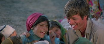 Movie still from “Caravans” (1978), directed by James Fargo – A man and two girls laughing together; Close Up shot, Over the shoulder angle