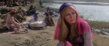 Movie still from “Caravans” (1978), directed by James Fargo – A woman with a veil sitting on the ground near a body of water; Medium shot, Low angle