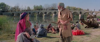 Movie still from “Caravans” (1978), directed by James Fargo – An old man holding a wooden stick in a field; Wide shot, Over the shoulder angle