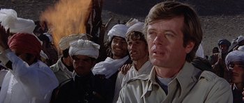 Movie still from “Caravans” (1978), directed by James Fargo – A group of men standing next to each other in front of a fire; Close Up shot, Low angle