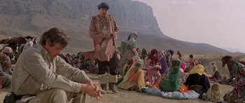 Movie still from “Caravans” (1978), directed by James Fargo – A group of people sitting in the desert; Wide shot, Over the shoulder angle