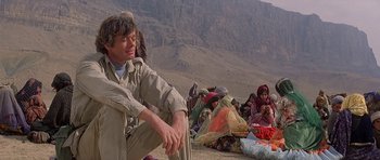 Movie still from “Caravans” (1978), directed by James Fargo – A man sitting on the ground next to a group of people; Medium shot, Low angle