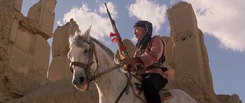 Movie still from “Caravans” (1978), directed by James Fargo – A man riding a horse with a rifle in his hand; Medium shot, Low angle