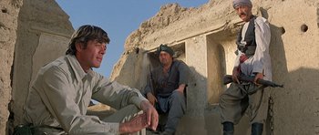 Movie still from “Caravans” (1978), directed by James Fargo – A group of men sitting on top of a rock wall; Medium shot, Low angle