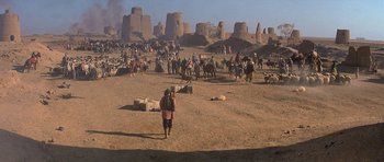 Movie still from “Caravans” (1978), directed by James Fargo – A group of people walking on a dirt field; Extreme Wide shot, High angle