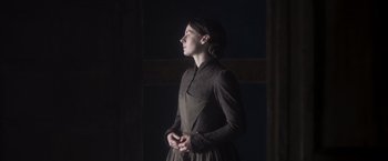 Movie still from “Carmilla” (2019), directed by Emily Harris – A woman in a dress standing in a dark room; Medium shot, Low angle