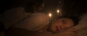 Movie still from “Carmilla” (2019), directed by Emily Harris – A woman laying on her stomach in a room with candles in the background; Close Up shot, High angle