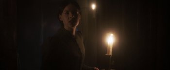 Movie still from “Carmilla” (2019), directed by Emily Harris – A woman holding a lit candle in a dark room; Medium shot, Low angle