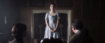Movie still from “Carmilla” (2019), directed by Emily Harris – A woman in a blue dress standing in front of a fireplace; Medium shot, Over the shoulder angle