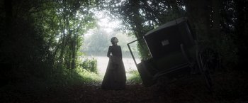Movie still from “Carmilla” (2019), directed by Emily Harris – A woman standing next to a tree in the woods; Wide shot, Low angle