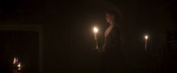 Movie still from “Carmilla” (2019), directed by Emily Harris – A woman holding a tray with a lit candle in the dark; Medium shot, Low angle