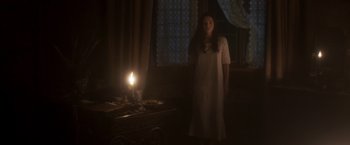 Movie still from “Carmilla” (2019), directed by Emily Harris – A woman standing in front of a lit candle in the dark; Wide shot, High angle