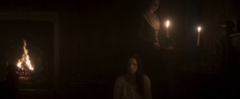 Movie still from “Carmilla” (2019), directed by Emily Harris – A woman standing next to another woman holding a lit candle; Medium shot, Low angle