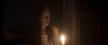 Movie still from “Carmilla” (2019), directed by Emily Harris – A woman standing next to a window with a lit candle in the dark; Close Up shot, Over the shoulder angle