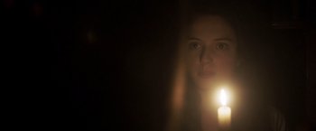 Movie still from “Carmilla” (2019), directed by Emily Harris – A woman is holding a candle in a dark room; Close Up shot, Low angle