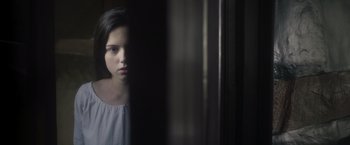 Movie still from “Carmilla” (2019), directed by Emily Harris – A young girl is standing in a dark room; Close Up shot, Low angle