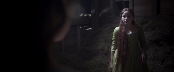 Movie still from “Carmilla” (2019), directed by Emily Harris – A woman with long red hair standing in a barn; Medium shot, Over the shoulder angle