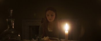 Movie still from “Carmilla” (2019), directed by Emily Harris – A woman sitting at a table with a plate of food and a lit candle; Medium shot, High angle