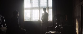 Movie still from “Carmilla” (2019), directed by Emily Harris – A woman standing in front of a window in a room; Wide shot, Over the shoulder angle