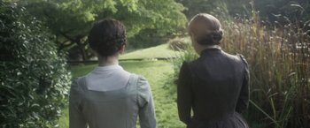 Movie still from “Carmilla” (2019), directed by Emily Harris – Two women are looking out over a lush green field; Medium shot, Over the shoulder angle