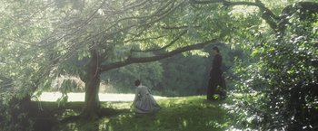 Movie still from “Carmilla” (2019), directed by Emily Harris – Two women in period dress sitting under a tree; Wide shot, High angle