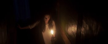 Movie still from “Carmilla” (2019), directed by Emily Harris – A woman holding a candle in a dark room; Medium shot, High angle