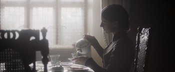 Movie still from “Carmilla” (2019), directed by Emily Harris – A woman sitting at a dining table pouring tea into a cup; Medium shot, Over the shoulder angle